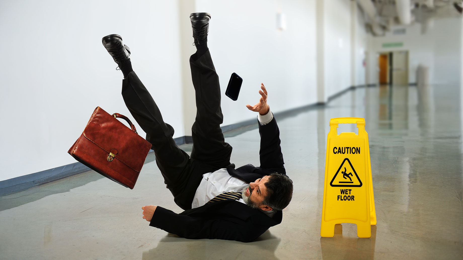 Businessman Slips and Falls Beside a Wet Floor Warning Sign