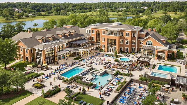 An aerial view of a luxurious assisted living facility featuring a gourmet dining area, modern fitness center, relaxing spa, and scenic outdoor areas for social activities and beautiful landscaping.