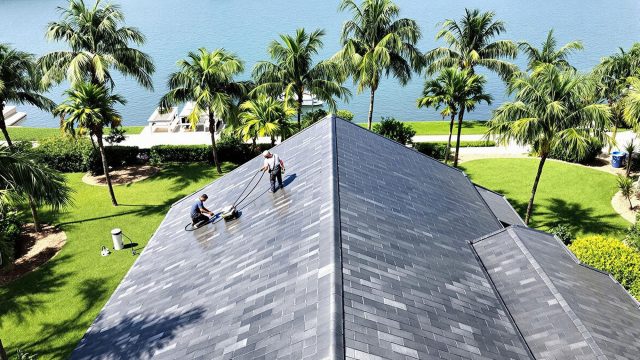 Professional soft wash roof cleaning in progress on a luxurious waterfront estate in Florida, showcasing well-maintained high-end roofing materials and a pristine coastal environment.