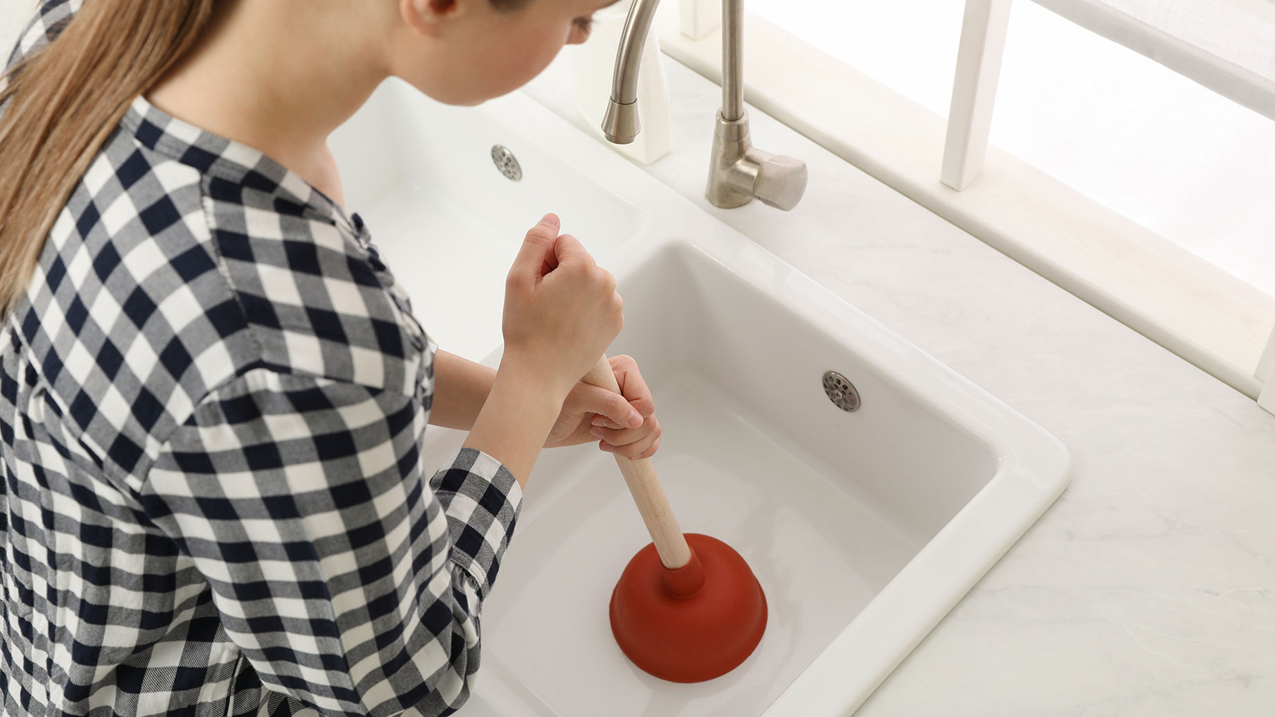 Woman Using a Plunger to Unclog a Sink