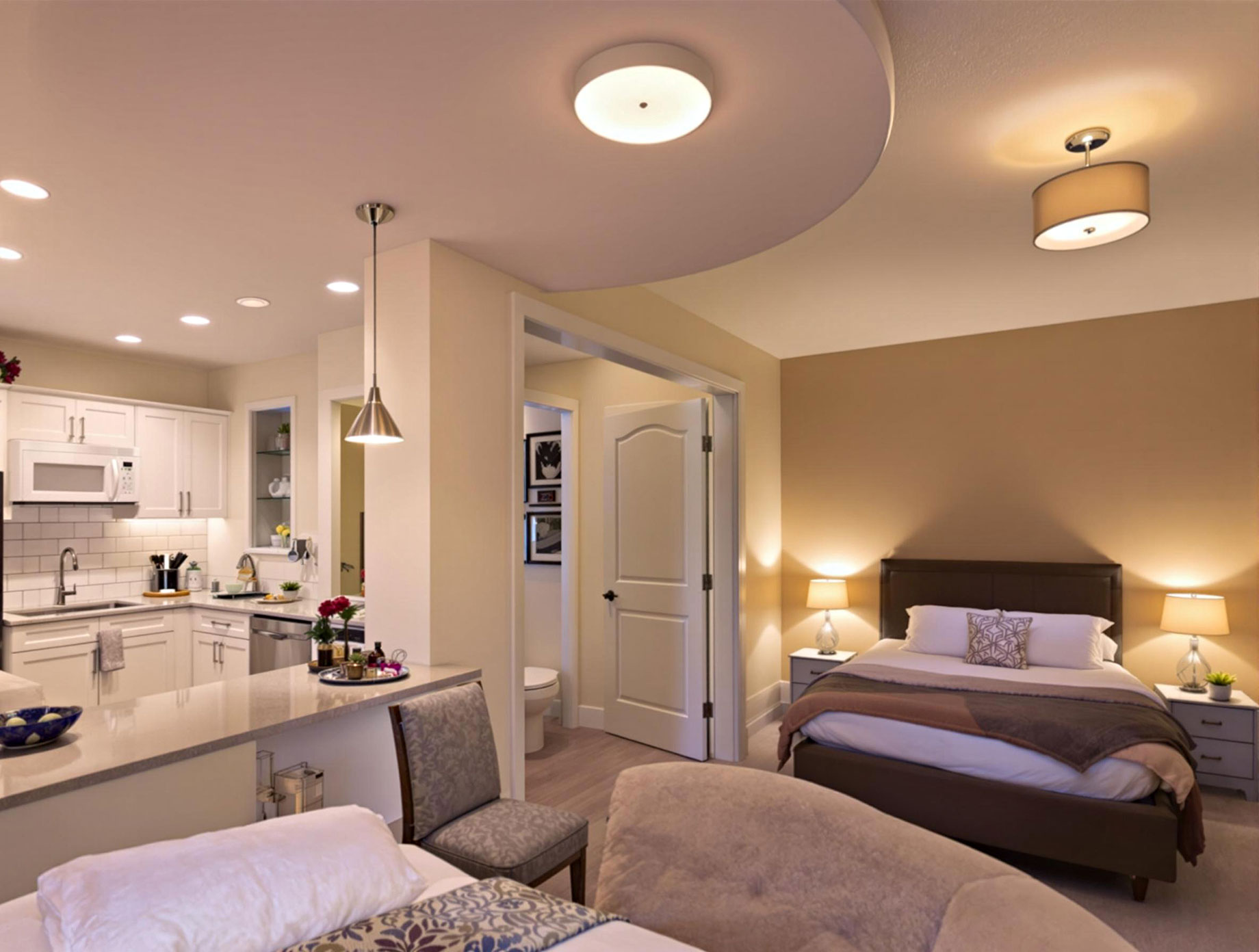 Showcasing a well-lit kitchen with overhead and under-cabinet lighting, a bathroom with ceiling and vanity lights, and a cozy bedroom with various lighting fixtures including table lamps and wall-mounted reading lights.