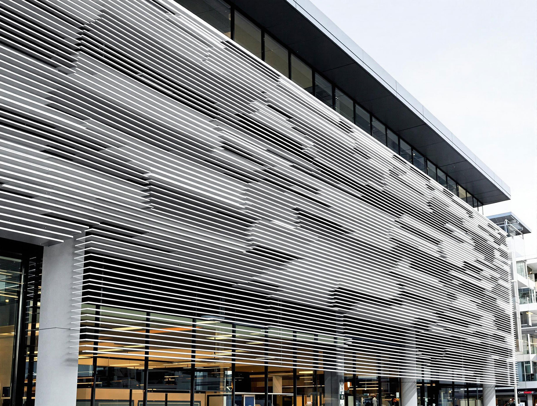 A modern building featuring aluminium batten cladding on its exterior façade. The linear aluminium profiles create dynamic shadow lines and visual texture, adding depth and architectural interest. The building is set in an urban environment, showcasing the material's versatility and aesthetic appeal in contemporary architecture.