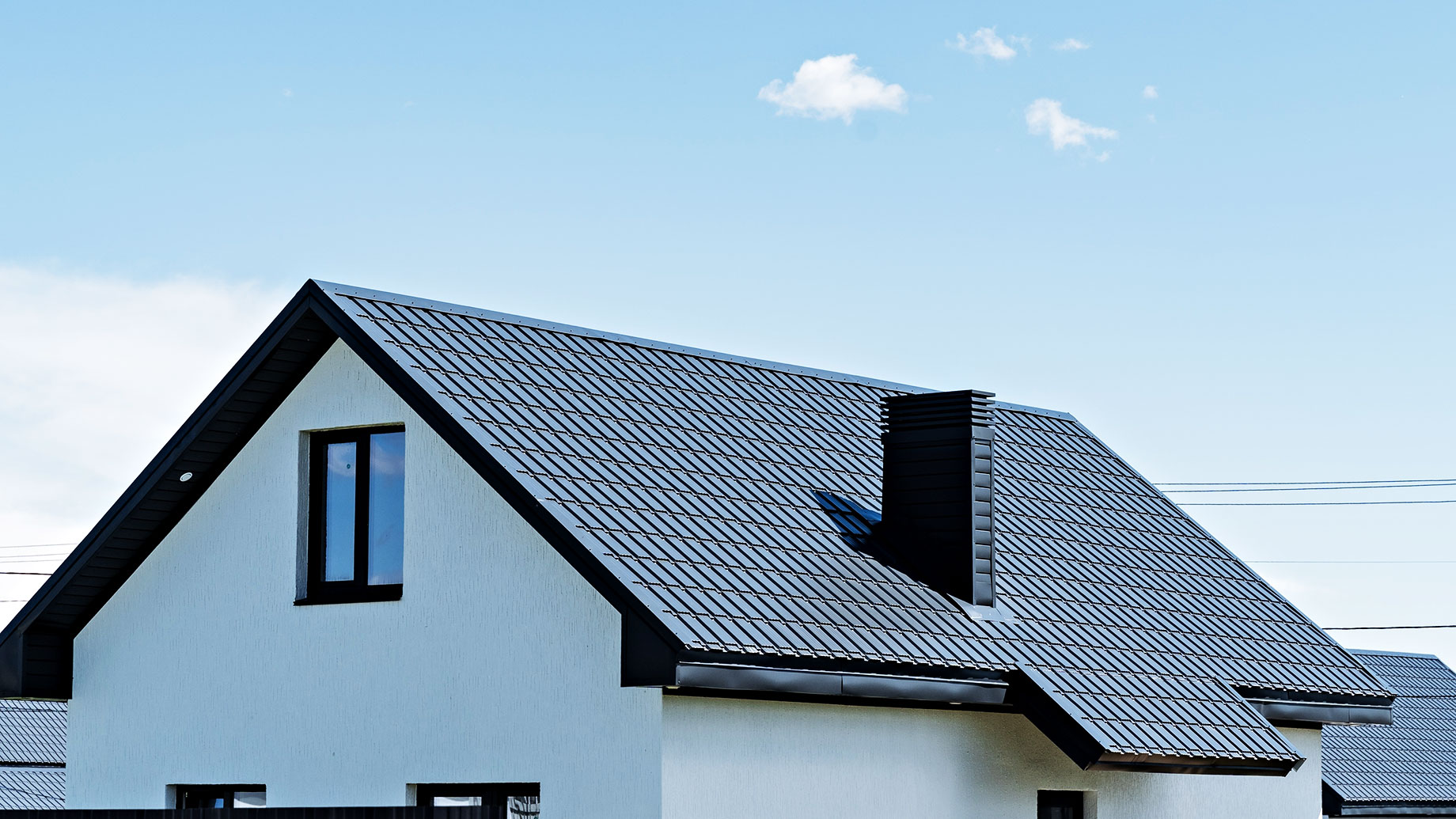 A modern house with a sleek, dark grey metal roof and a small attic window under a clear blue sky.