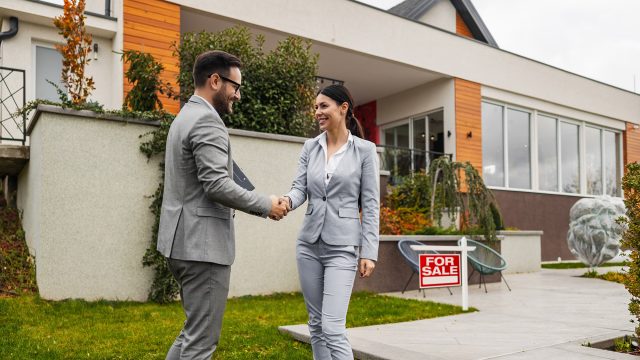 Real Estate Agent and Client Shaking Hands in Front of a Home For Sale