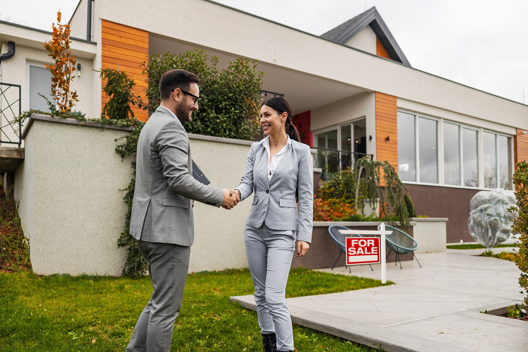 Real Estate Agent and Client Shaking Hands in Front of a Home For Sale
