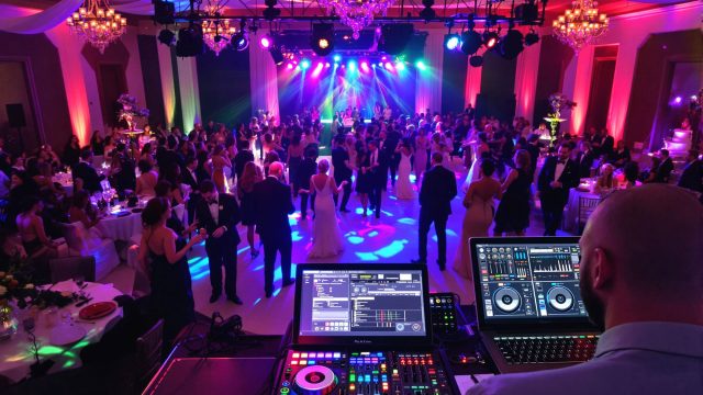 A lively wedding reception with a professional DJ at the booth, surrounded by guests dancing and enjoying the festive atmosphere, highlighting the importance of selecting the right DJ for an unforgettable experience.