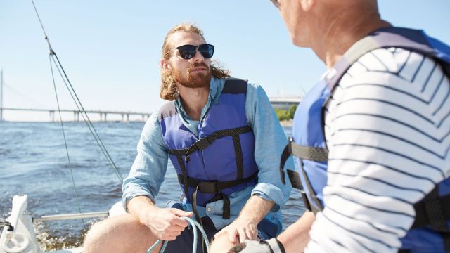 Two men wearing life jackets discussing boating safety on a sailboat, highlighting beginner boating training and boat club safety support in Florida.