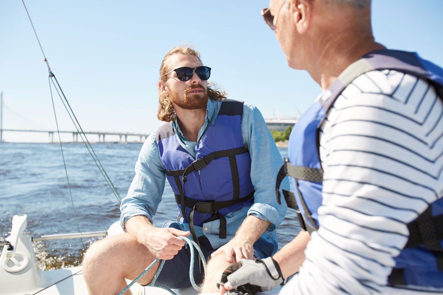 Two men wearing life jackets discussing boating safety on a sailboat, highlighting beginner boating training and boat club safety support in Florida.