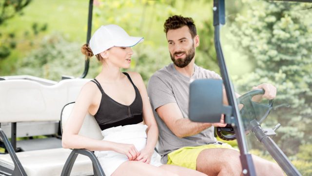Couple riding a golf cart in summer outfits, surrounded by greenery — outdoor leisure and resort lifestyle scene.