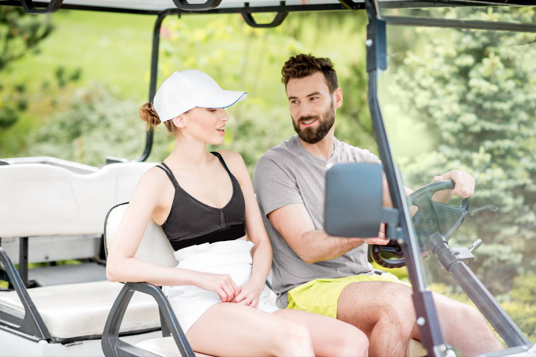 Couple riding a golf cart in summer outfits, surrounded by greenery — outdoor leisure and resort lifestyle scene.