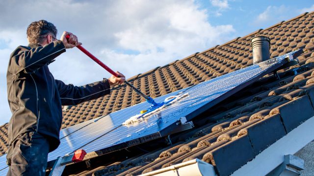 Man Cleaning Solar Panels on the Roof