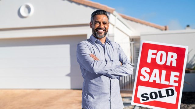 Man Standing Beside a House for Sale with a Sold Sticker