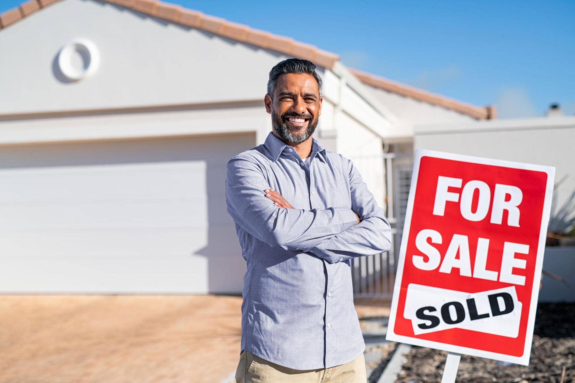 Man Standing Beside a House for Sale with a Sold Sticker