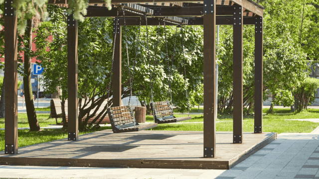 A shaded wooden pergola with two hanging swings in a landscaped green area, showcasing a relaxing outdoor feature in a luxury community.