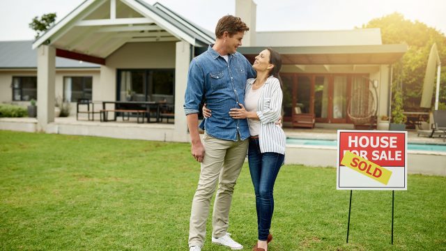 Couple in Front of a Home with a House for Sale Sign and Sold Sticker