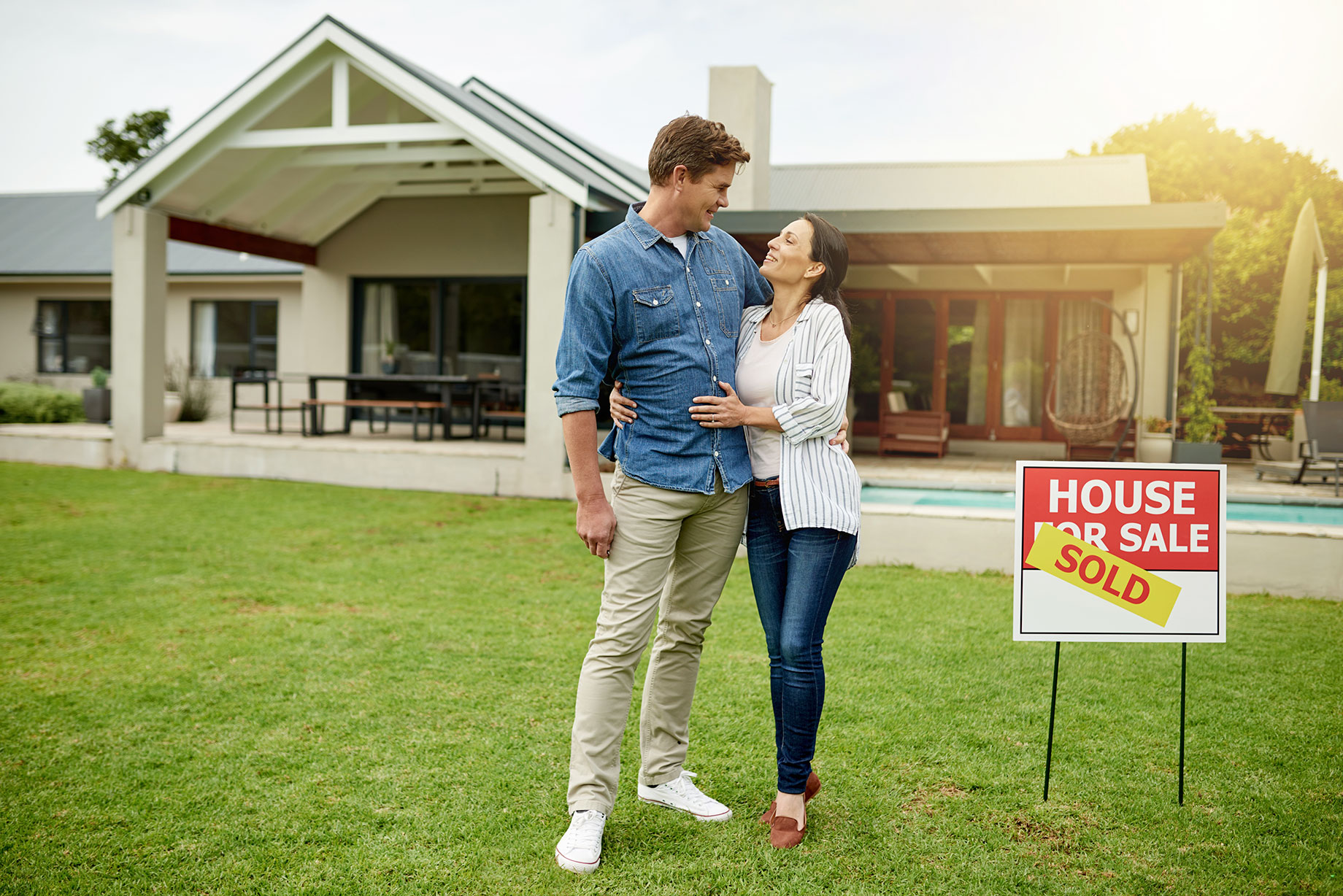 Couple in Front of a Home with a House for Sale Sign and Sold Sticker