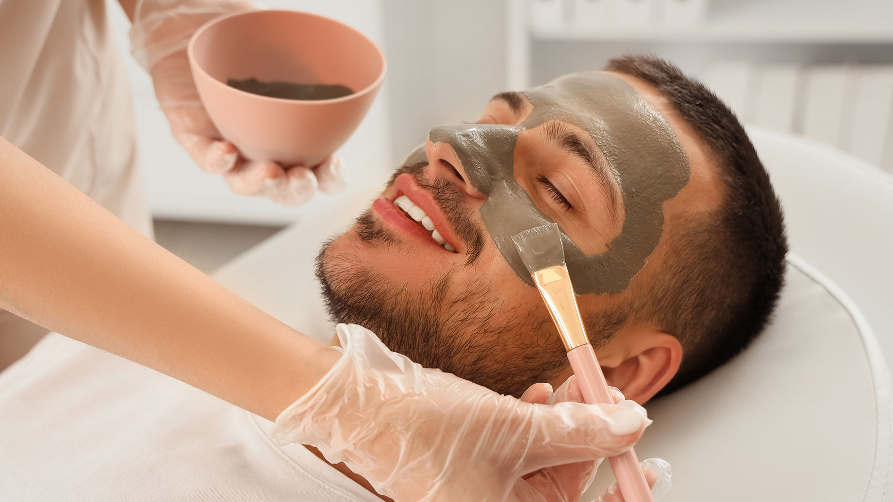 Beautician Applying Cosmetic Clay Mask on a Man's Face in Spa Salon