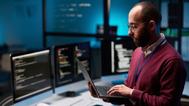 Computer Programmer Holding Open Laptop in IT and Cybersecurity Office