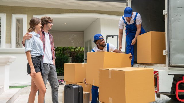 Moving Company Professionals Packing the Truck with the Moving Couple Looking On