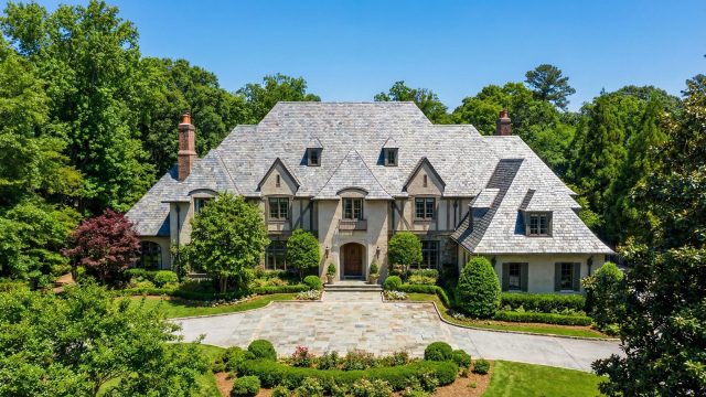 Front exterior view of a large luxury home in Atlanta featuring a complex slate roof design, stone driveway, and lush landscaping, showcasing high-end residential roofing.