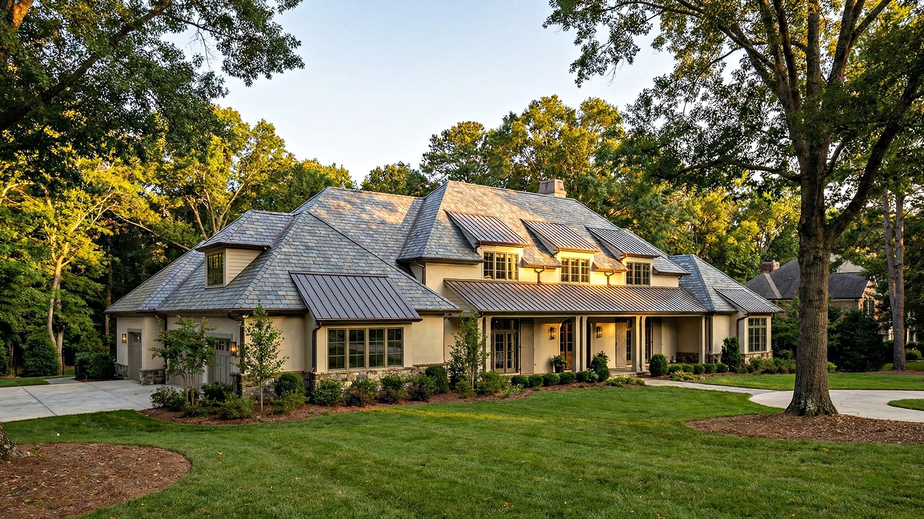 Exterior of a sprawling luxury home in Raleigh, North Carolina, showcasing expert craftsmanship with a durable slate and metal roof system amidst a landscape of mature oak trees.