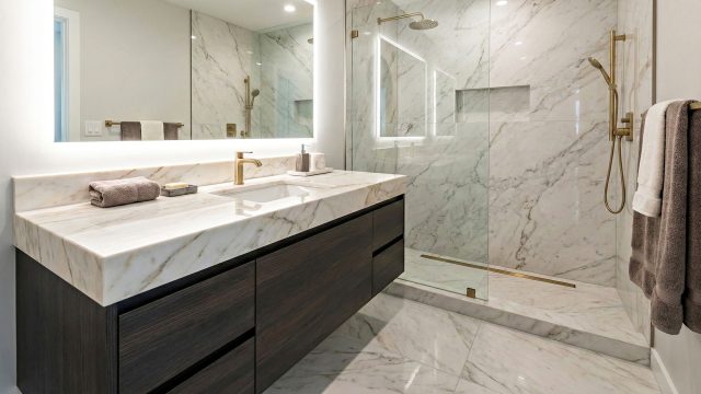 A spacious, high-end modern bathroom showcasing durable remodeling materials, including large-format porcelain floor tiles, a sleek white quartz vanity countertop, and a seamless glass shower enclosure; the design combines spa-like elegance with water-resistant practicality.
