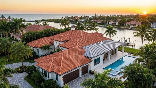 Aerial view of a luxury waterfront estate at sunset featuring a pristine terracotta clay tile roof with modern standing seam metal accents, illustrating the high-quality craftsmanship expected from top roofers in Central and Southwest Florida.