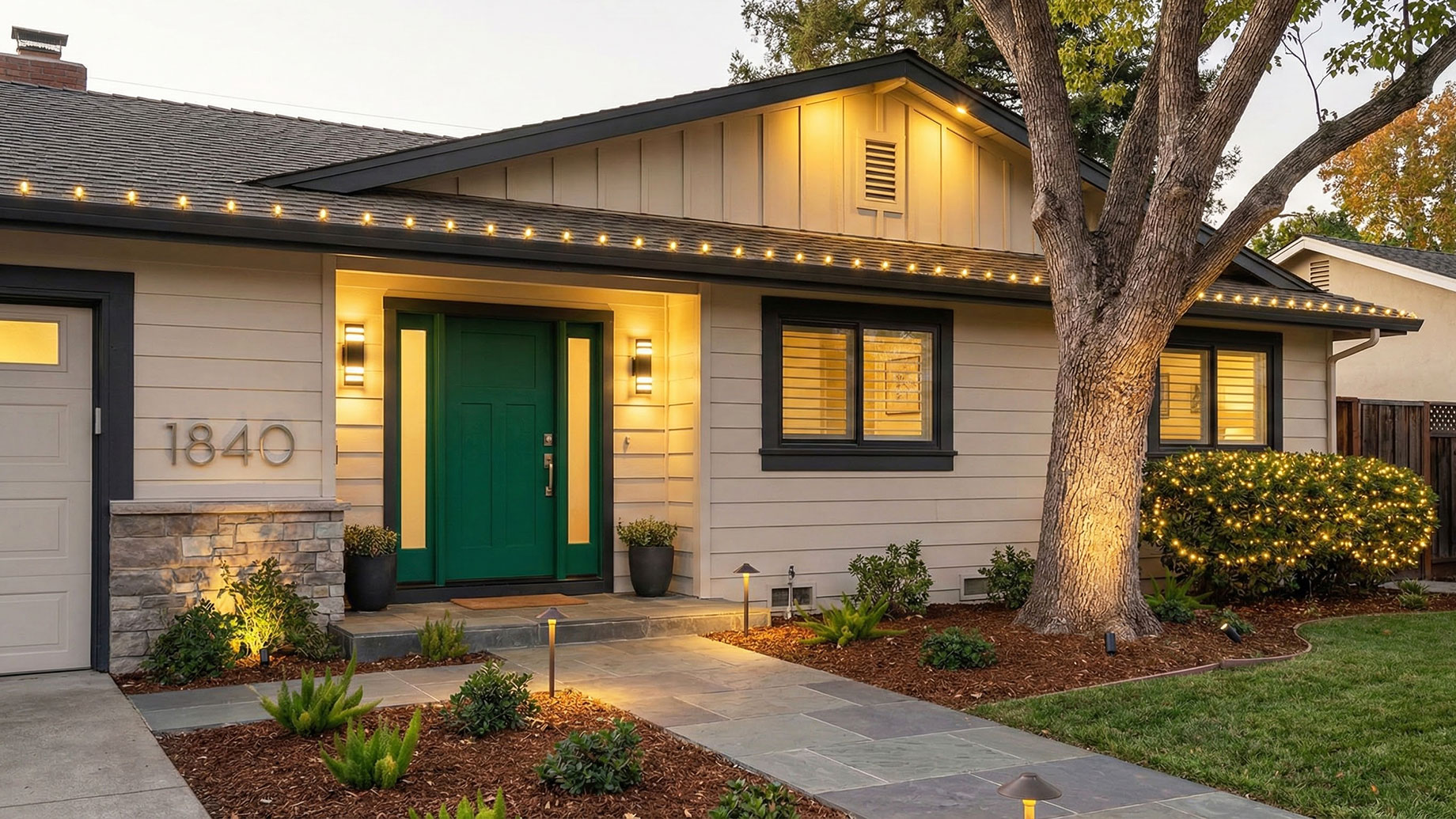 A renovated home exterior featuring high-impact updates, including dark contrasting trim against beige siding, an emerald green front door, modern floating address numbers, and warm holiday string lights along the roofline.