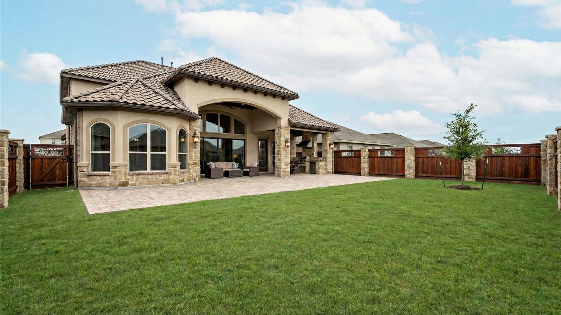 A wide, high-angle shot of a large, empty backyard of a luxury modern home featuring a manicured flat green lawn, a high-end horizontal wood slat privacy fence, and expansive glass windows, illustrating a space that feels vacant despite its size.