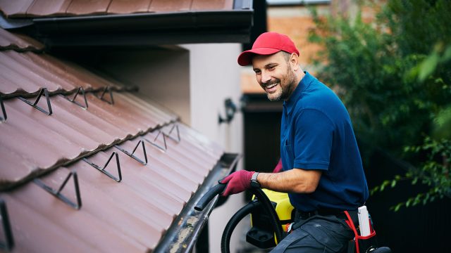 Professional Gutter Maintenance Worker Blowing Leaves Out Of A Gutter