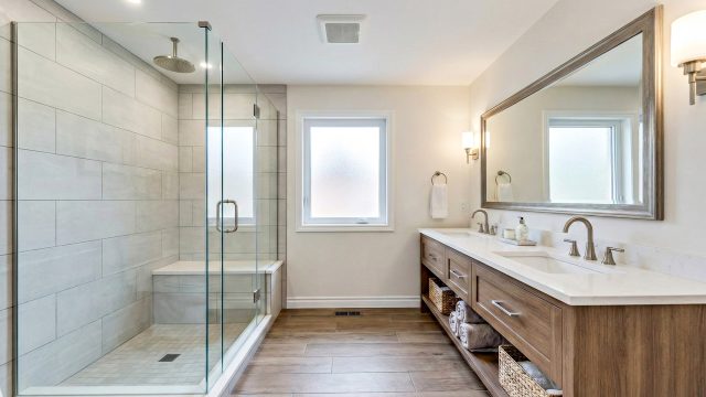 A bright, modern bathroom featuring a spacious glass walk-in shower with neutral tiling, a natural wood double vanity with organized storage, and soft layered lighting, showcasing high-value home upgrades.
