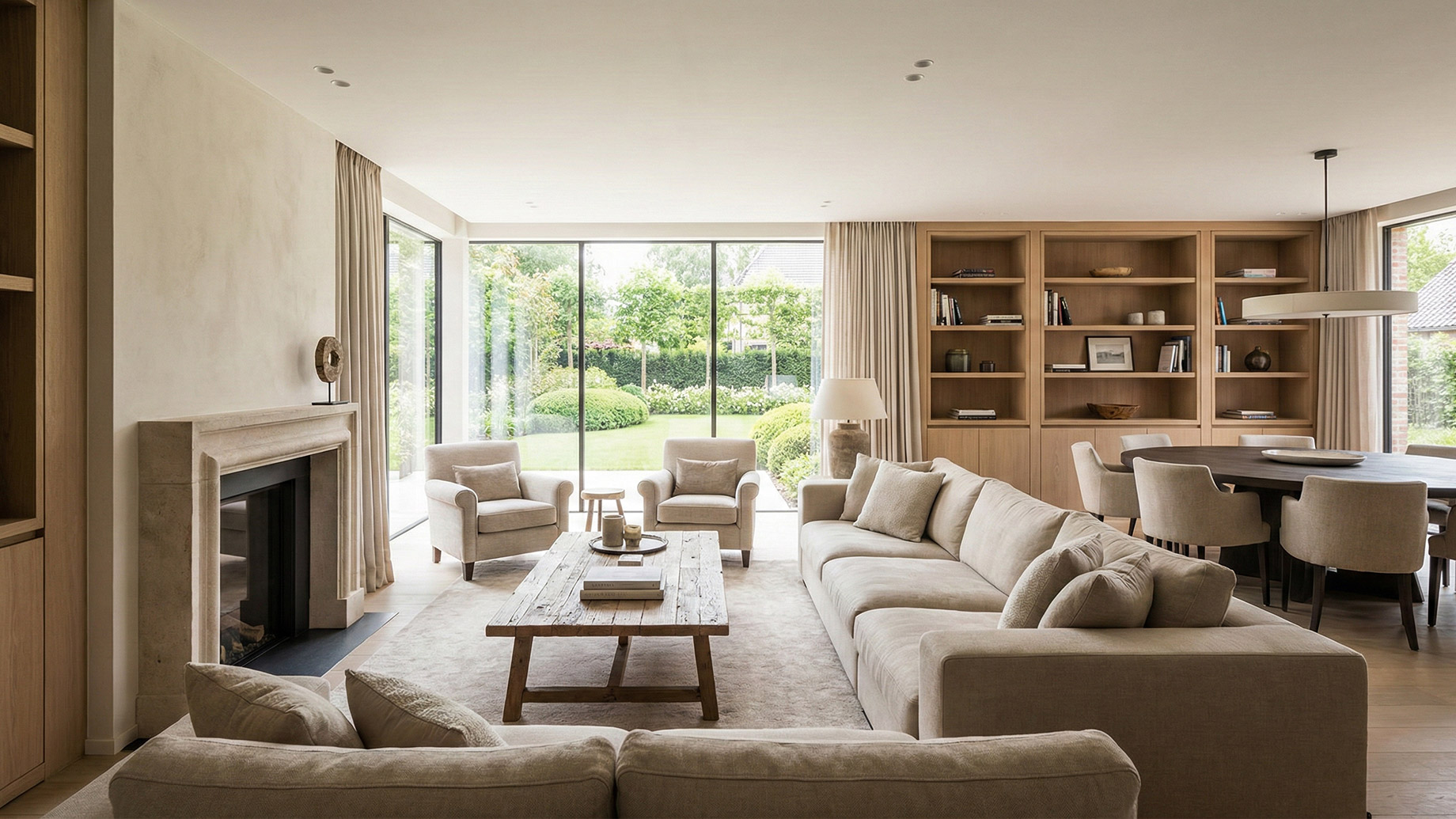 A wide shot of a luxurious, open-concept living room bathed in natural light from large floor-to-ceiling windows overlooking a garden. The space features a neutral color palette with beige furniture and warm wood accents, a large sectional sofa, and built-in shelving that seamlessly flows into a dining area, illustrating a balance of comfort and practicality.