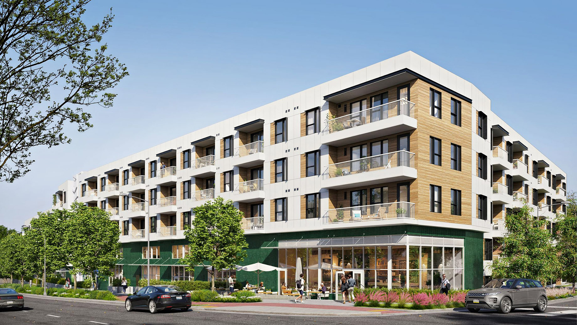 A street-level architectural view of The Code, a modern five-story hybrid hotel-residence building located at 2323 South Lamar Boulevard in Austin, Texas. The exterior features a contemporary mix of white paneling and warm, horizontal wood siding, with numerous glass-railed balconies for the 178 fully furnished units. The ground floor is highlighted by a deep green facade and a large glass-fronted on-site café where people are gathered at outdoor tables under white umbrellas. Lush green trees and modern vehicles line the street under a bright, clear sky.