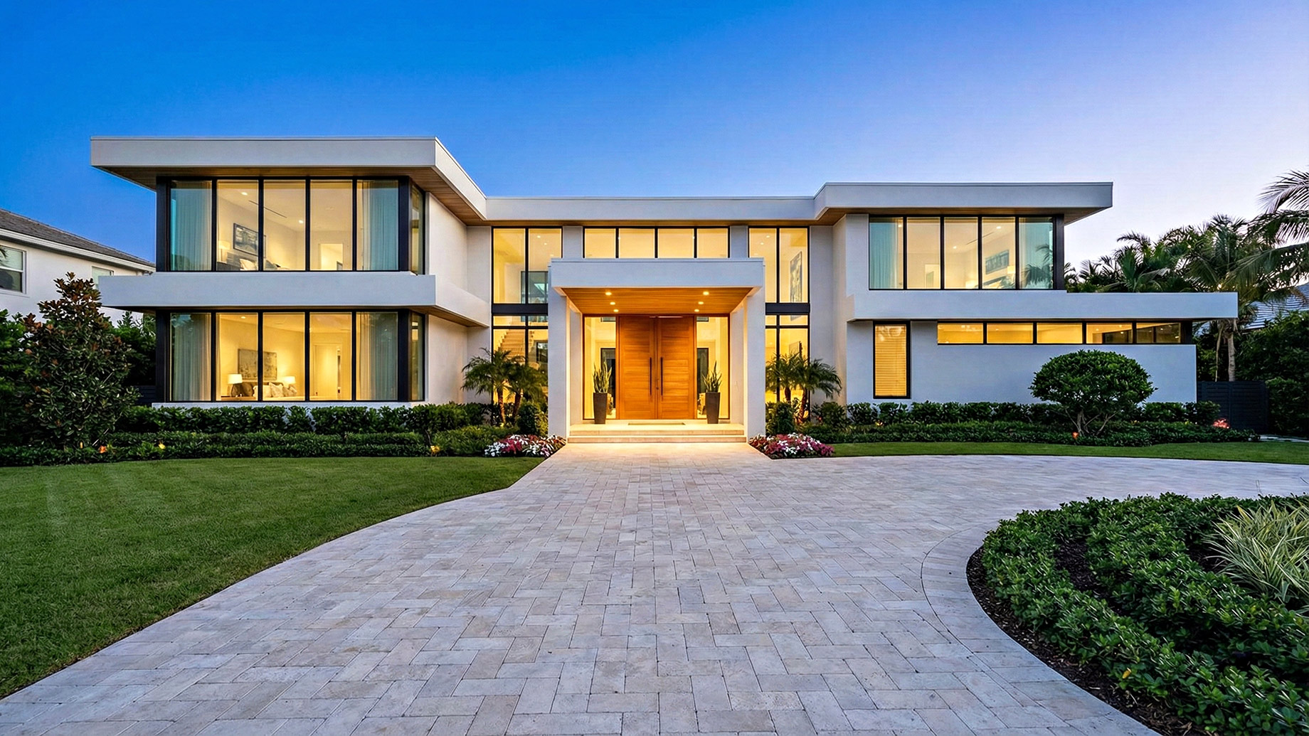 A modern luxury home at twilight featuring a spotless, freshly cleaned paver driveway and gleaming white exterior surfaces, illustrating the high curb appeal of well-maintained property exteriors.