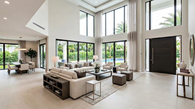 A spacious luxury living room featuring high ceilings, floor-to-ceiling windows, and clean neutral furniture, demonstrating a perfectly staged home ready for a quick sale.