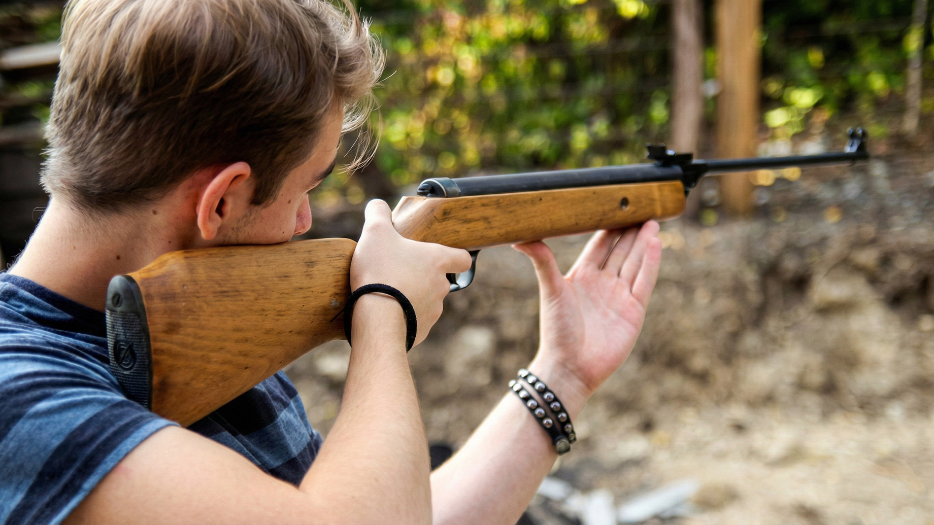 An individual outdoors aiming a traditional wooden-stock rifle, looking down the barrel during a target practice session.