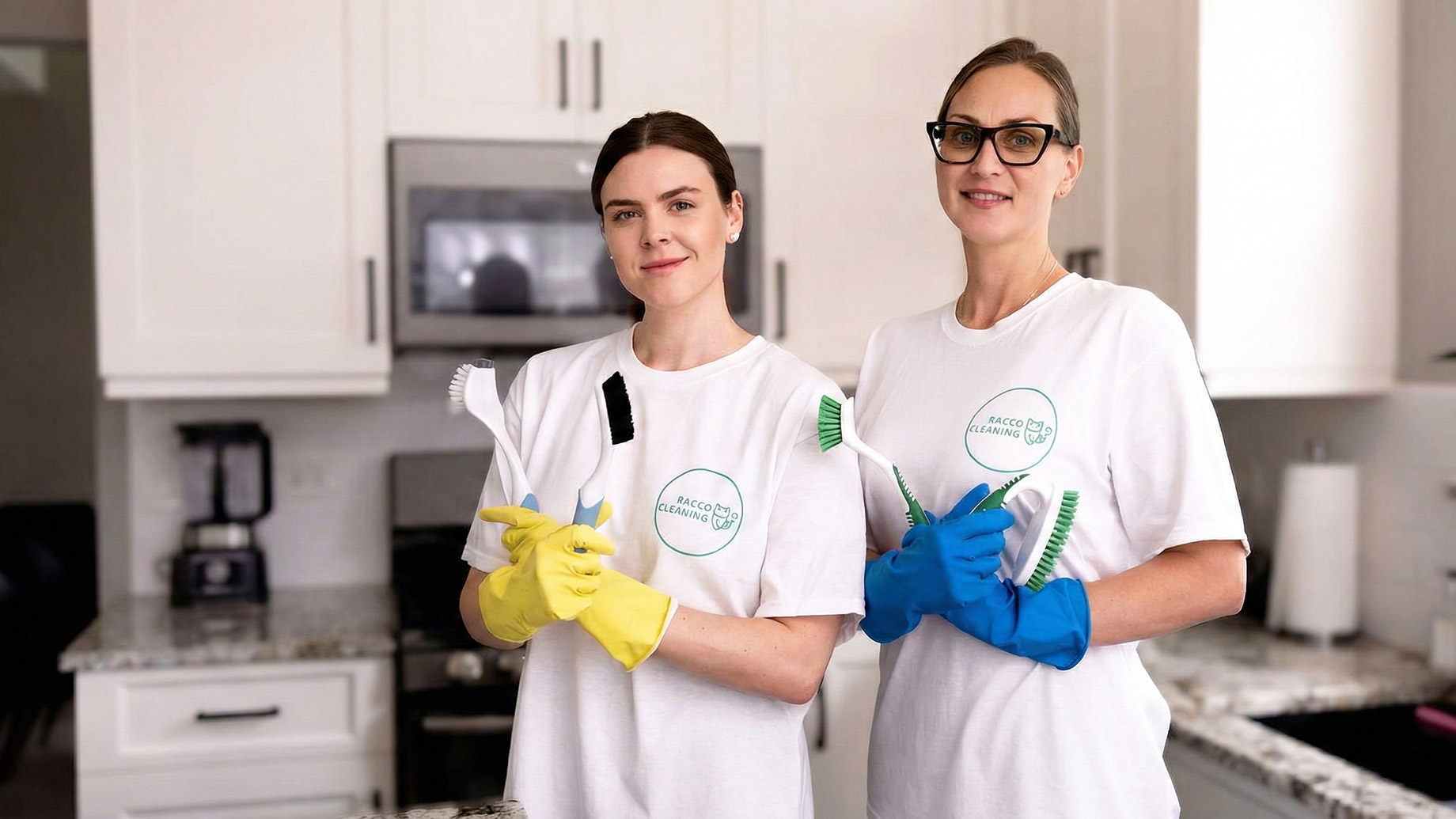 Two women from Raccoon Cleaning, wearing white branded t-shirts and gloves, stand in a kitchen holding cleaning brushes, representing the company's commitment to integrating eco-friendly practices into everyday cleaning operations.