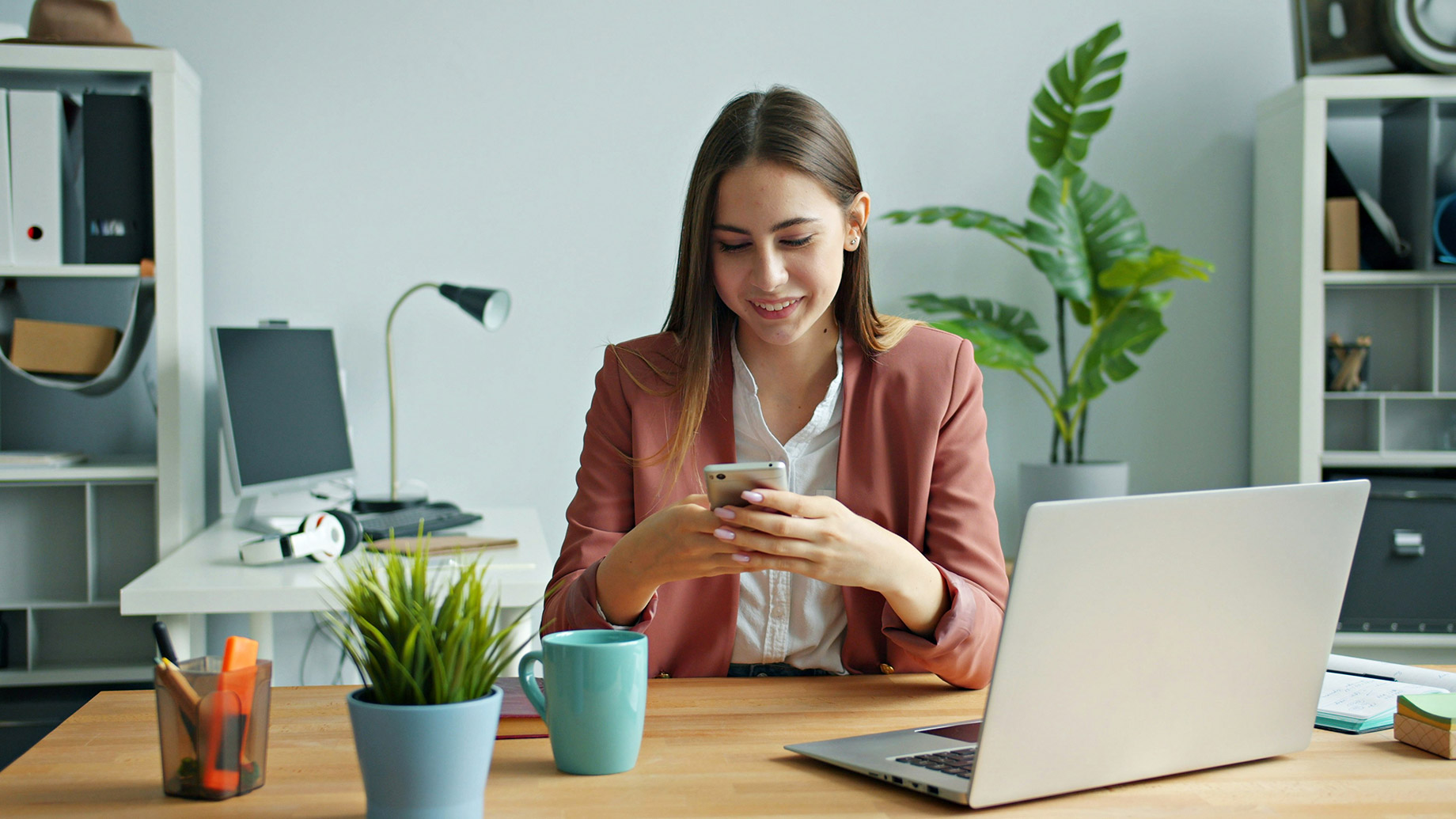 Young Woman Smiling While Using Her Smartphone at Desk