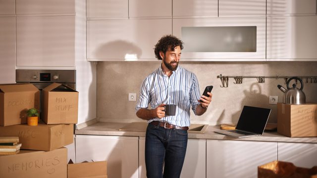A Man Stands in a Bright Kitchen Filled With Moving Boxes