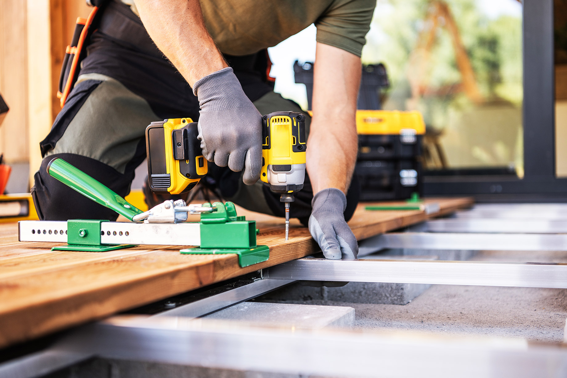 A contractor using a power drill to fasten wooden deck boards on a frame while building a custom outdoor deck.