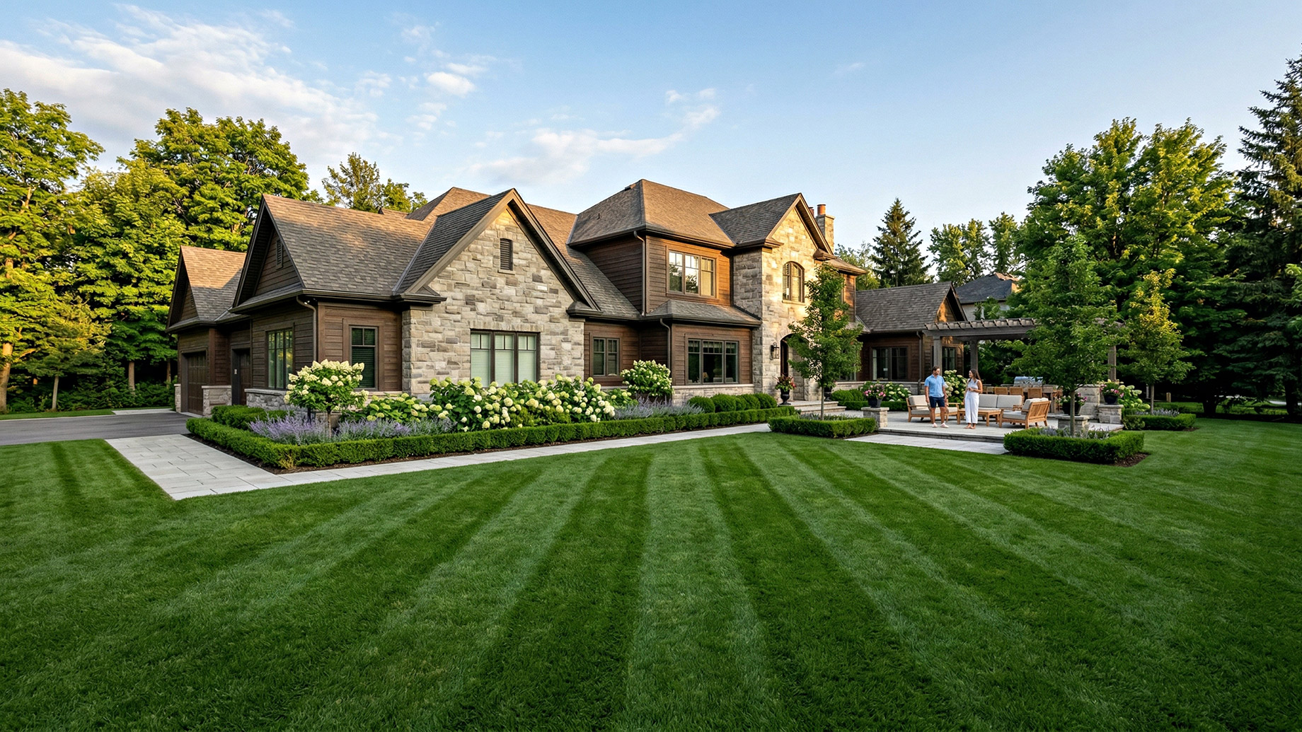 A large stone and wood craftsman mansion with a massive, perfectly striped green lawn and manicured garden beds.