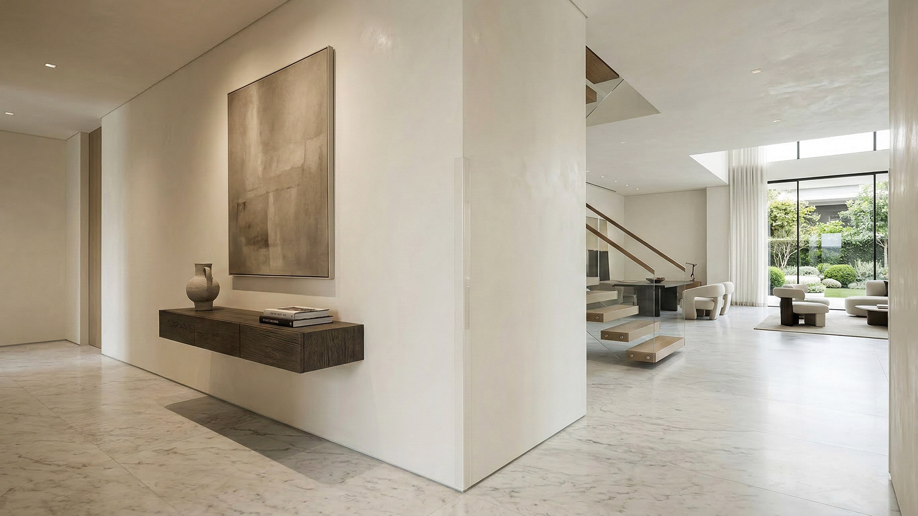 A bright, minimalist luxury interior featuring a prominent white wall corner fitted with a clear, nearly invisible edge protector. To the left is a floating wooden console under an abstract painting; to the right, marble floors lead toward a glass-paneled staircase and a sunlit living area with floor-to-ceiling windows.
