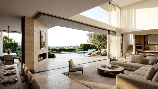 A vast, modern open-plan living and dining area in a luxury villa, where fully retracted floor-to-ceiling glass doors create a seamless connection to an expansive stone pool deck and a distant, sprawling coastal city skyline under a clear, sunny sky.