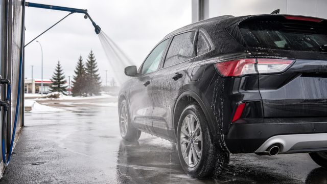 Black SUV being rinsed with high-pressure water in a car wash bay during snowy winter conditions in Central Alberta.