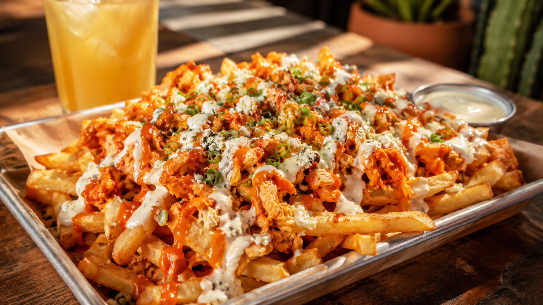 Loaded buffalo chicken fries topped with spicy buffalo sauce, ranch, crumbled cheese, and green onions on a metal tray.
