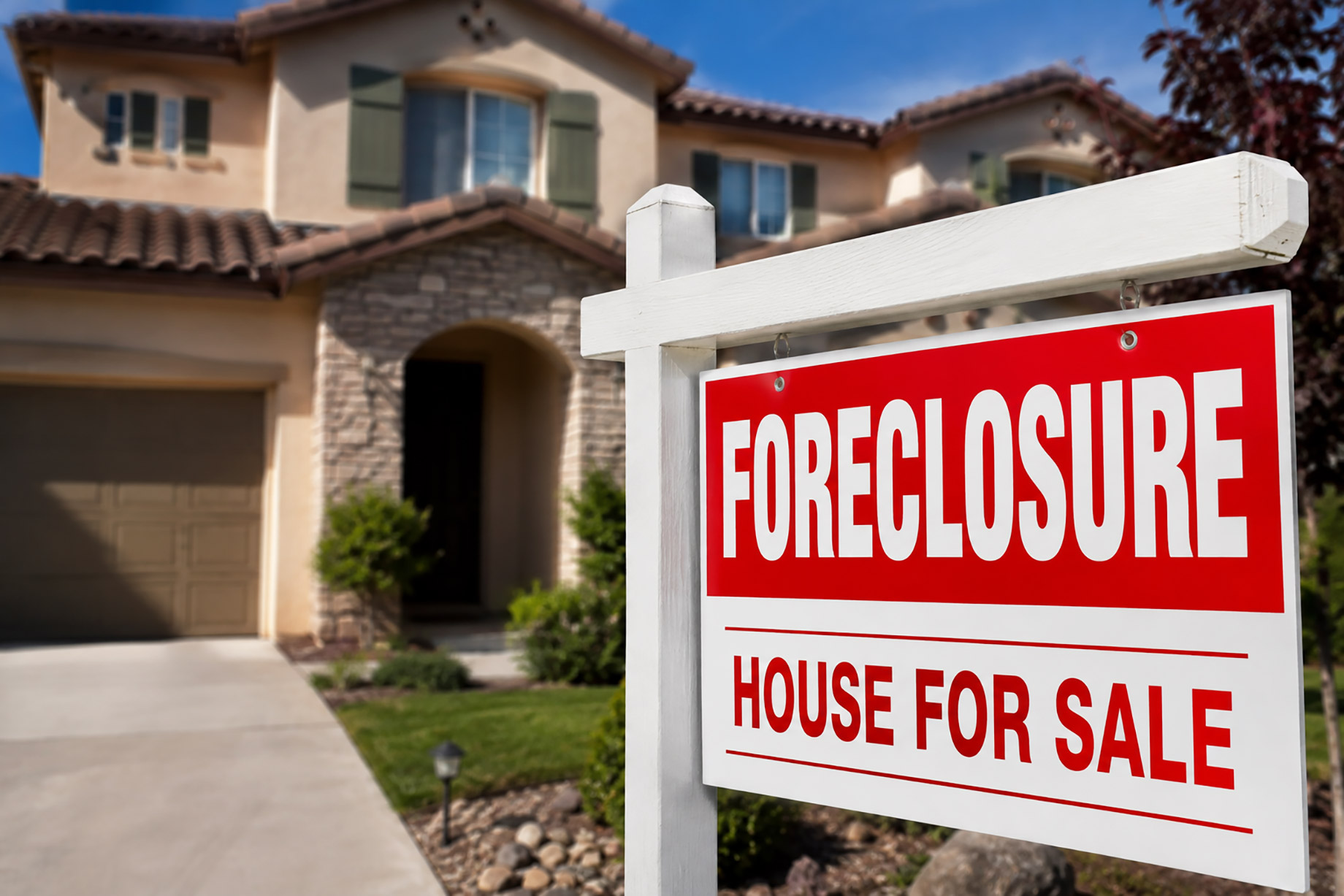 Red and white foreclosure house for sale sign in front of a suburban California home with tan stucco, tile roofing, landscaped yard, and bright blue sky.