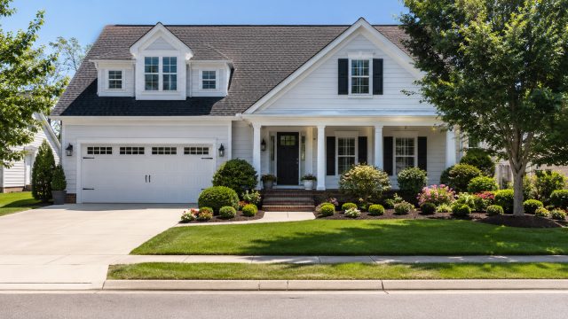 A bright white suburban home with clean siding, sharp lawn edges, trimmed landscaping, fresh garden beds, and a spotless driveway on a sunny street.
