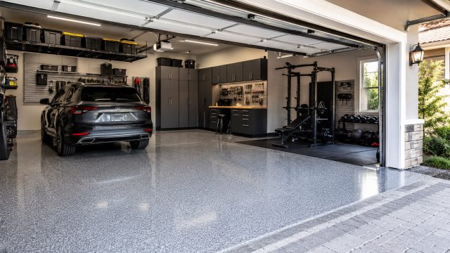 Modern two-car garage with polished concrete coating, organized storage cabinets, overhead shelving, parked SUV, and home gym area.