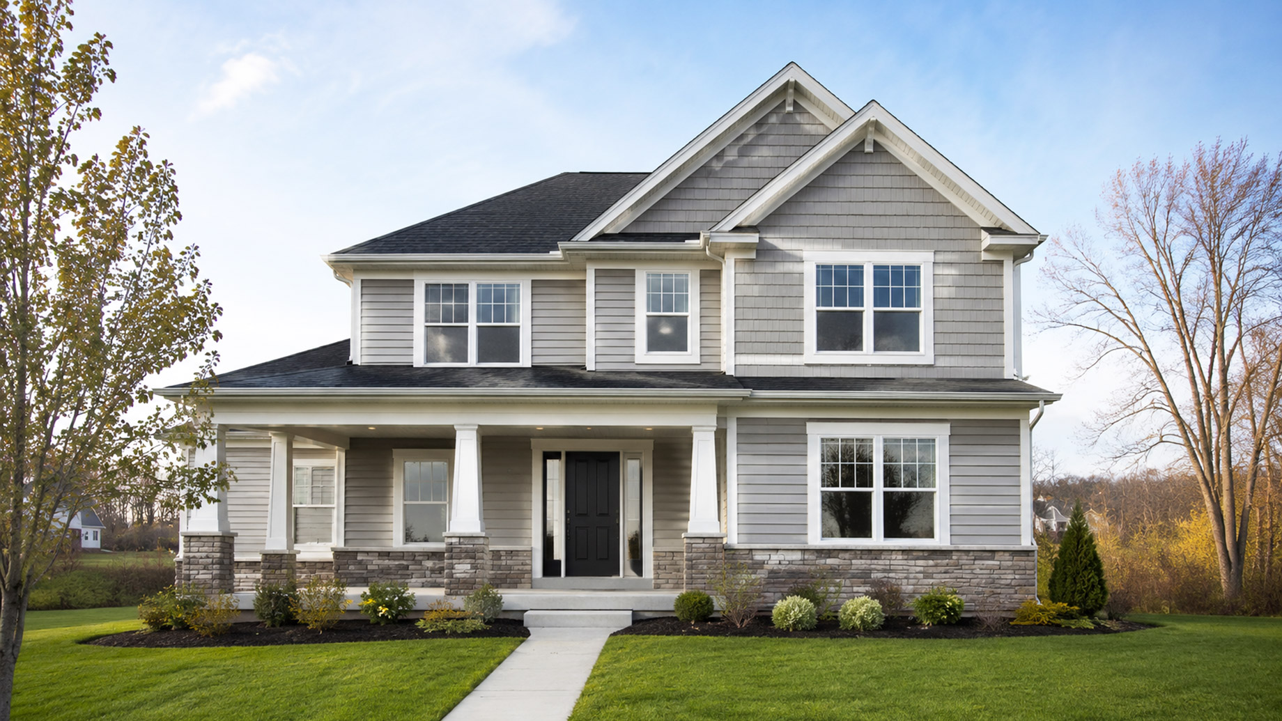 A two-story suburban home in Northern Indiana features clean grey siding, white trim, stone accents, a covered front porch, and a neatly maintained lawn.