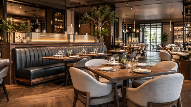 Upscale modern restaurant interior with upholstered dining chairs, wood tables, booth seating, warm lighting, and refined commercial furniture.